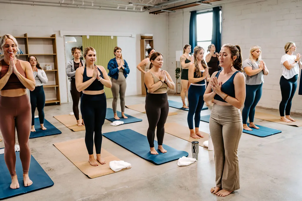 A Sunday Studio class standing on their mats with hands at heart